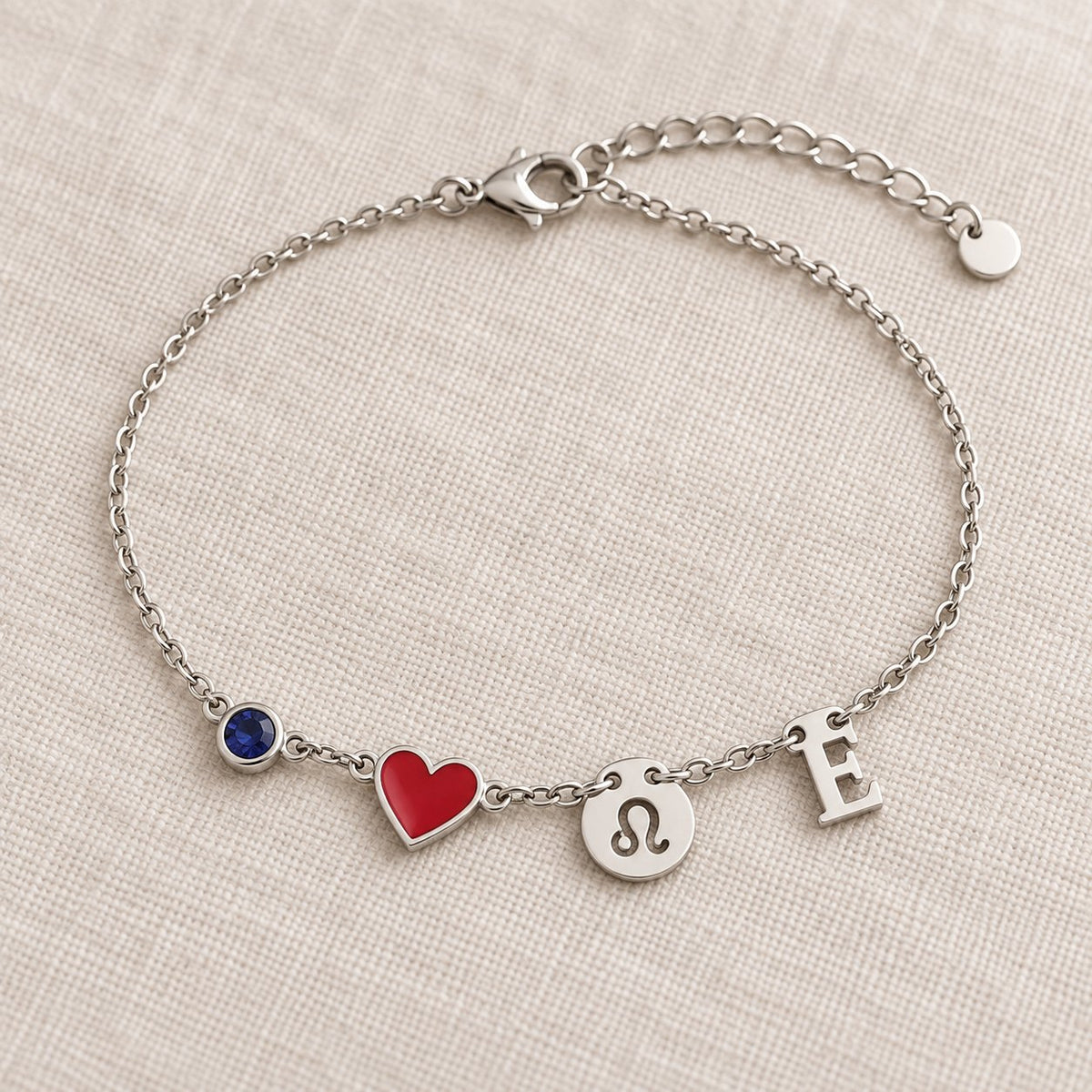 Bracelet Olianne finition argentée : pierre bleue de septembre, cœur rouge, signe Lion et initiale E